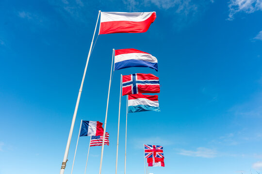 Utah Beach, France - 10 June 2026: View of multiple national flags waving against a clear blue sky at the historic site of Utah Beach.