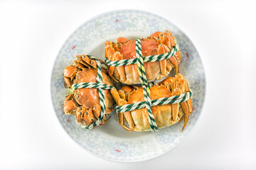 Three cooked crabs secured with string, placed on a decorative ceramic plate, presented against a plain white background. © tai