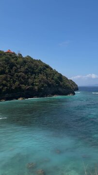 A serene coastal view featuring a lush green hill beside clear turquoise waters under a bright blue sky. Ideal for travel and nature themes.