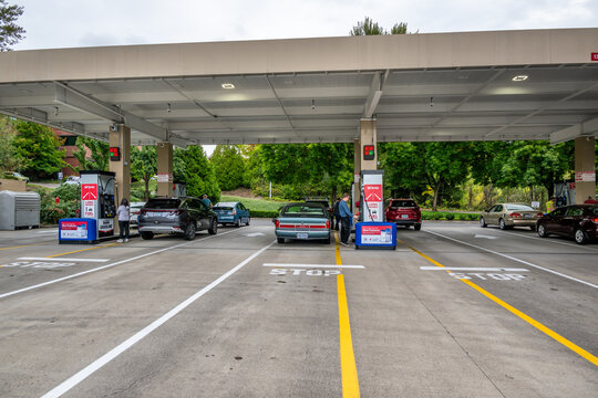 Portland, Oregon, United States - 15 September 2026: View of Costco gas station with cars refueling under a large canopy, people standing by pumps, and green trees in the background.