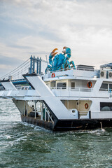 Fototapeta premium Moored vessel with a blue crab sculpture and bridge behind. A crab sculpture sits on a white vessel in New York City, with a steel suspension bridge in the background.