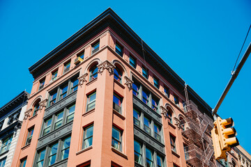 Upward view of an ornate corner facade and traffic signal. Arched windows and carved details frame a brick corner in New York City beneath a clear blue sky. © Vadim
