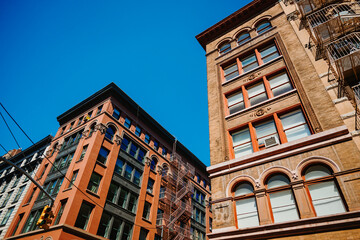 Brick facades framing a clear sky above a street corner. Arched windows and metal stairs rise on both sides of a street corner in New York City. © Vadim