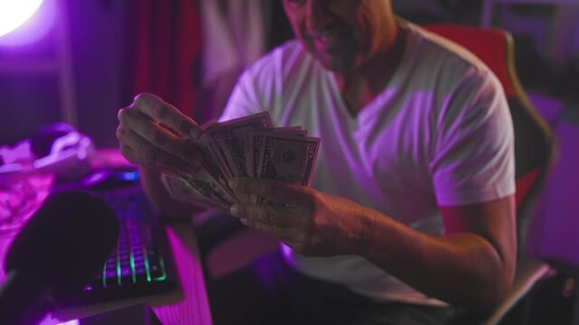 Man fanning dollars with hands in studio near keyboard and microphone under purple light; confident focus.