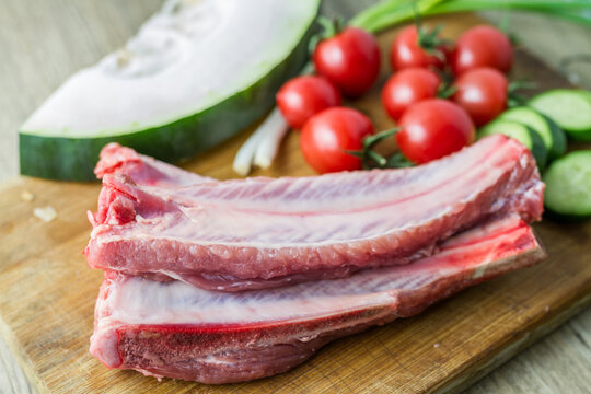 Raw pork ribs paired with fresh vegetables arranged on a wooden cutting board, ready for cooking preparation.