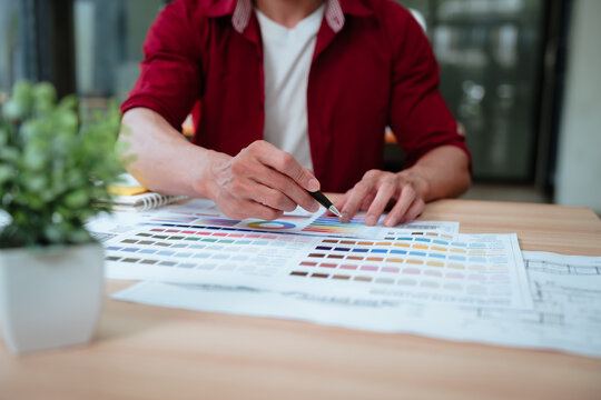 Creative designer reviewing color palettes, architectural concepts, and visual plans on a computer in a modern workspace.