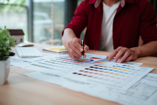 Creative designer reviewing color palettes, architectural concepts, and visual plans on a computer in a modern workspace.