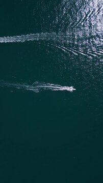 Aerial top down view of two motorboats speeding across deep blue ocean water
