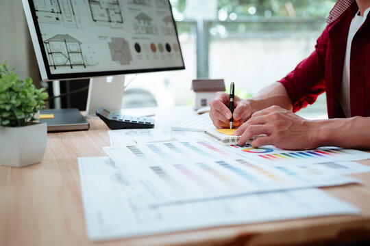 Creative designer reviewing color palettes, architectural concepts, and visual plans on a computer in a modern workspace.