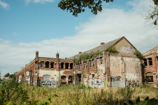 Leipzig, Saxony, Germany - 15 September 2026: View of an abandoned industrial building with weathered red brick walls, graffiti, broken windows, and overgrown vegetation.