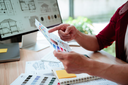 Creative designer reviewing color palettes, architectural concepts, and visual plans on a computer in a modern workspace.
