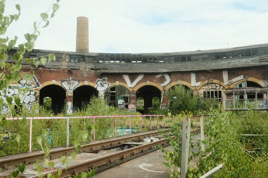 Leipzig, Germany - 15 September 2026: View of the abandoned roundhouse in Leipzig, featuring weathered brick arches with graffiti, overgrown railway tracks, and a tall chimney.