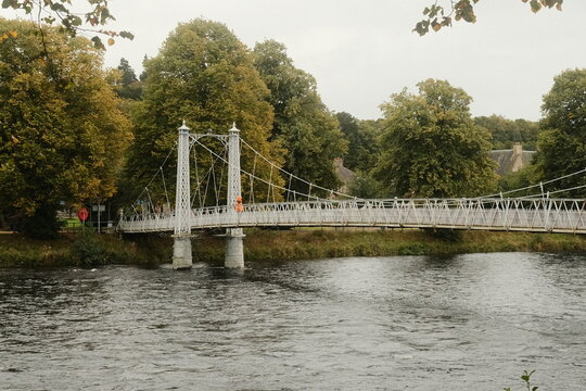 Inverness, United Kingdom - 17 September 2026: View of the historic white suspension bridge crossing the River Ness, surrounded by lush green trees on a calm day.