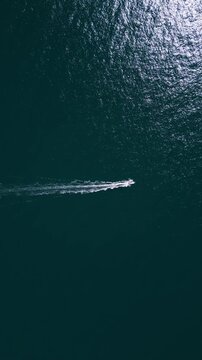 Aerial top down view of a motorboat speeding across deep blue ocean water
