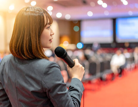 Professional woman speaking into a microphone at a large corporate business conference event