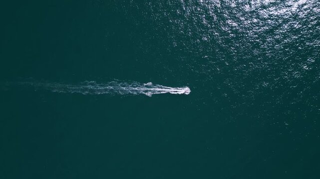 Aerial top down view of a motorboat speeding across deep blue ocean water