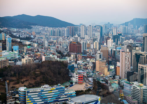 Busan, South Korea - 07 February 2026: View of the dense urban cityscape of Busan, featuring high-rise buildings, residential blocks, and hilly terrain under a soft evening sky.