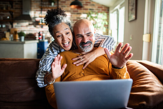 Happy senior couple waving on a video call at home