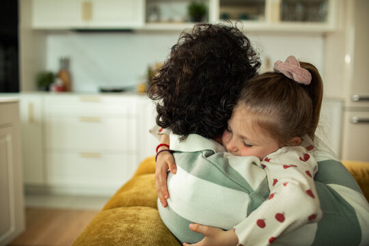 Little girl hugging parent in home kitchen