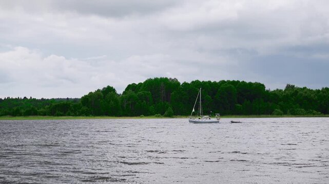White yacht sailing on Lake Onega with forest shore and cloudy sky, Karelia northern landscape