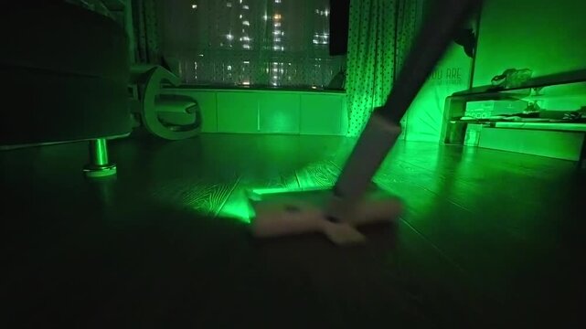 Vacuum cleaner using green light to reveal dust on dark floor.   