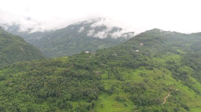 Aerial drone view of a misty forested hillside with scattered village houses fading into low hanging cloud Nepal