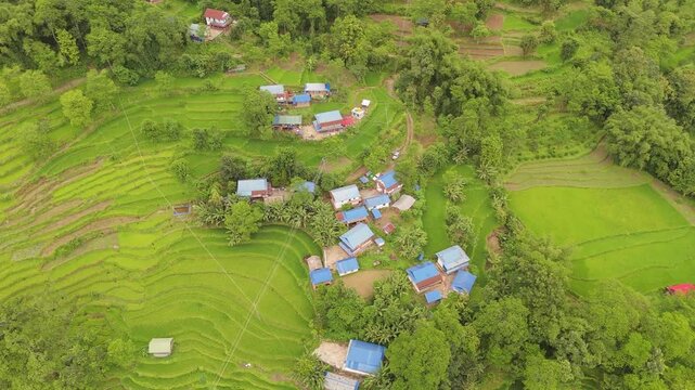 Drone shot of a dense rural hamlet with many blue and red rooftops nestled among green terraces Nepal