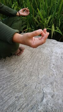 Person practicing yoga meditation while sitting on a stone surface outdoors in nature.