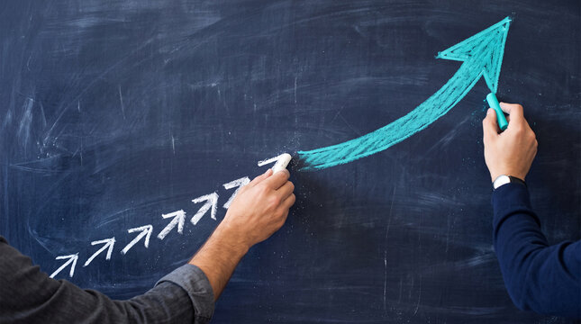 Hands drawing an upward trending arrow on a chalkboard, symbolizing growth, progress, and success in business and learning