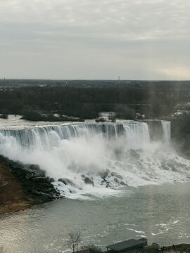 Niagara Falls, Ontario, Canada - 22 December 2023: View of Niagara Falls with cascading water, rocky riverbanks, and a cloudy winter sky.