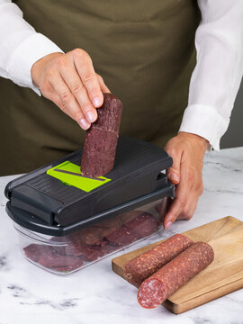 A woman slices dry-cured sausage using a manual vegetable cutter with a transparent container