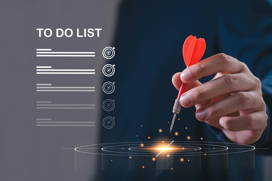 Hand holding a red dart over a glowing target with a digital task list, symbolizing goal setting, focus, productivity, task management, planning, priorities, achievement, and business success.