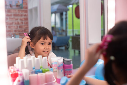 Young girl brushing her hair in a pretend beauty salon, looking at her reflection in a mirror while enjoying creative roleplay that develops imagination, confidence, independence, self-expression.