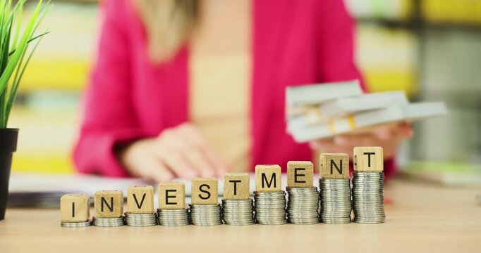 Entrepreneur places bundles of dollar banknotes on table. Wooden blocks form word Investment on coins steps as symbol of financial plans. Slow motion