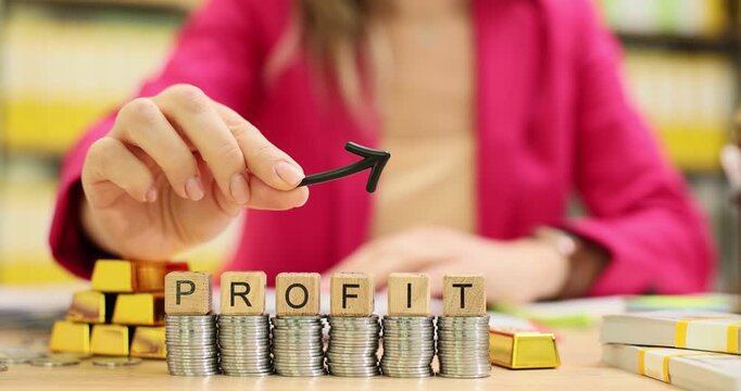 Executive holds small upward arrow to indicate increase in revenue. Neatly positioned wooden cubes form word Profit on office table. Slow motion