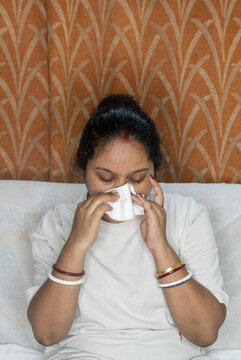 Indian young woman sick, suffering from fever and cold flu on sitting sofa, blowing on her nose with napkin or tissue, Pollen allergy, sneezing, flu fever concept.