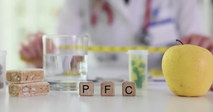 Letters PFC for proteins fats and carbohydrates on wooden blocks. Woman dietician holds tape measure over table with apple water pills and snacks