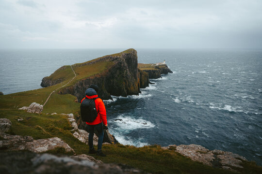 Portree, Scotland, United Kingdom - 10 November 2022: View of a photographer in an orange jacket standing on cliffs overlooking Neist Point Lighthouse and the rugged coastline.