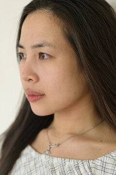 Close-up portrait of a young woman with long dark hair and natural makeup looking thoughtfully to the side