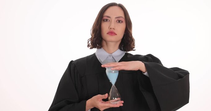 Serious woman judge in judicial robe turns over hourglass. Lawyer emphasizes approaching end of important legal deadline against white background