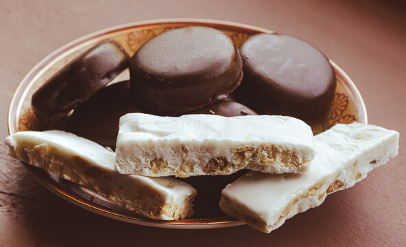 Traditional Spanish turron and chocolate cookies on a decorative plate, offering sweet holiday treats with a mix of soft nougat and rich cocoa, isolated .