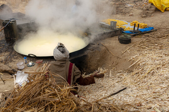 Multan, Punjab, Pakistan - 25 January 2013: View of a worker preparing traditional jaggery in a large boiling vat amidst piles of sugarcane bagasse in an outdoor setting.