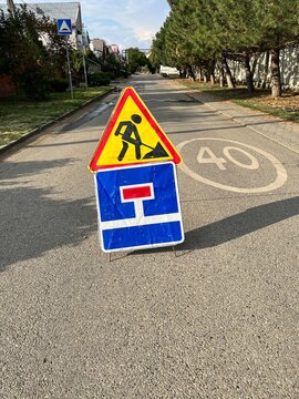 Worn yellow men at work and blue dead end signs on asphalt street with painted speed limit marking. Workers ahead