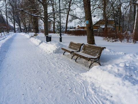 View of two wooden benches on a snow-covered path in the park of Traku Voke manor in Vilnius, Vilniaus apskritis, Lithuania.