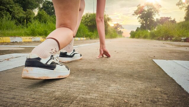 Runner in starting position on road at sunrise wearing white sneakers and socks symbolizing readiness motivation and beginning of journey