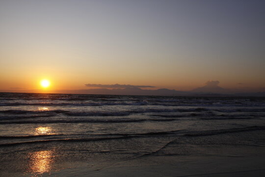 Golden sun setting over ocean horizon with gentle waves crashing