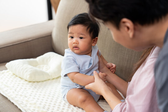 An Asian mother shares a close bonding moment with her baby at home while the father remains nearby, highlighting maternal care, family affection, gentle interaction, and everyday parenthood.