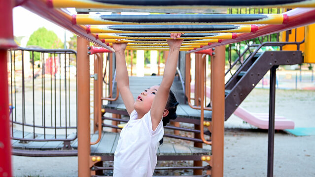 Young girl climbing and playing on monkey bars at a public playground, enjoying outdoor recreation and physical activity.