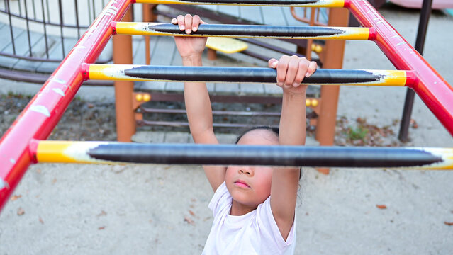 Young girl climbing and playing on monkey bars at a public playground, enjoying outdoor recreation and physical activity.
