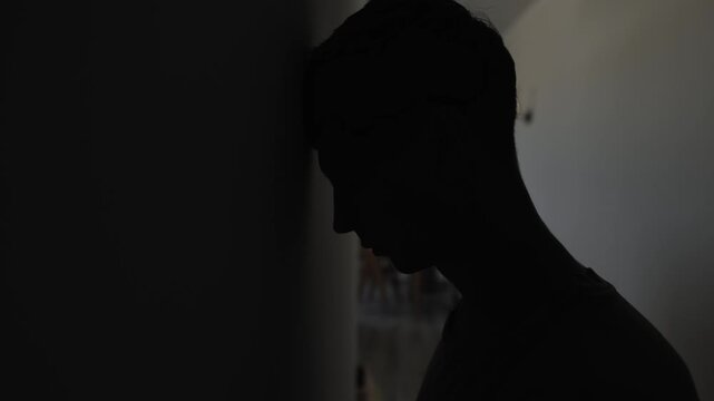 Desperate man hitting head against wall with dark copy space